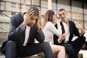 a distressed man holding his head in his hands as two employees speak with each other