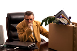 disgruntled man sitting behind a desk with a box full of his office materials in it