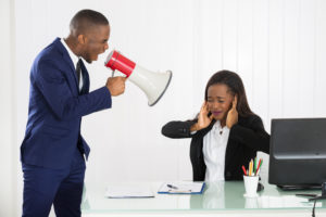 angry boss using a megaphone to shout at a female employee who's covering her aers