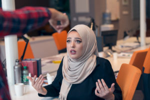 woman wearing a hijab with an unbelievable look on her face as an employer points her to leave