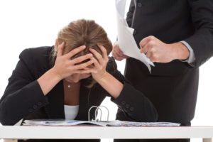 angry boss yelling at an employee as she cradles her head in her hands