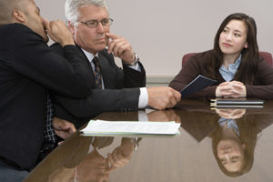 two older business men whispering to each other while a young Asian applicant sits at the edge of the table