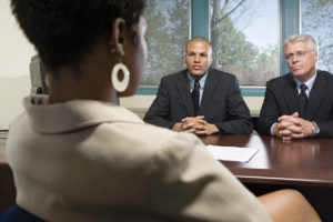 African American woman sitting in at a job interview as two businessmen look at her judgmentally