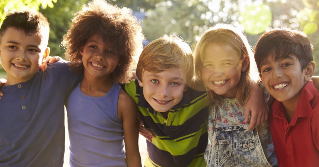 five children hugging outside as the sun sets in the background