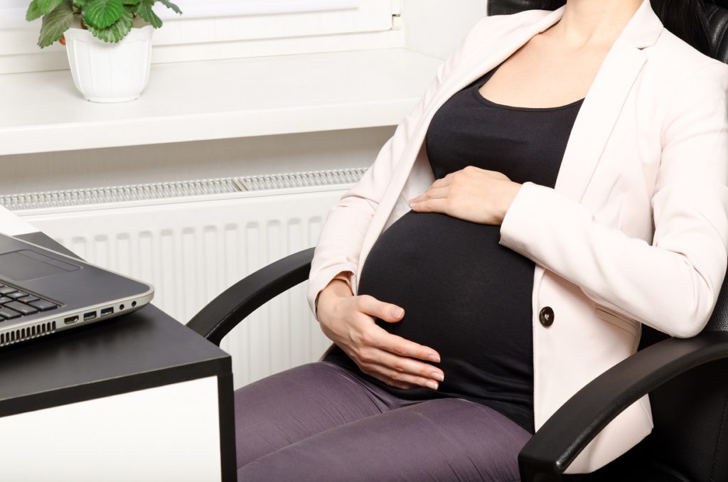 close up of pregnant belly in front of laptop at work